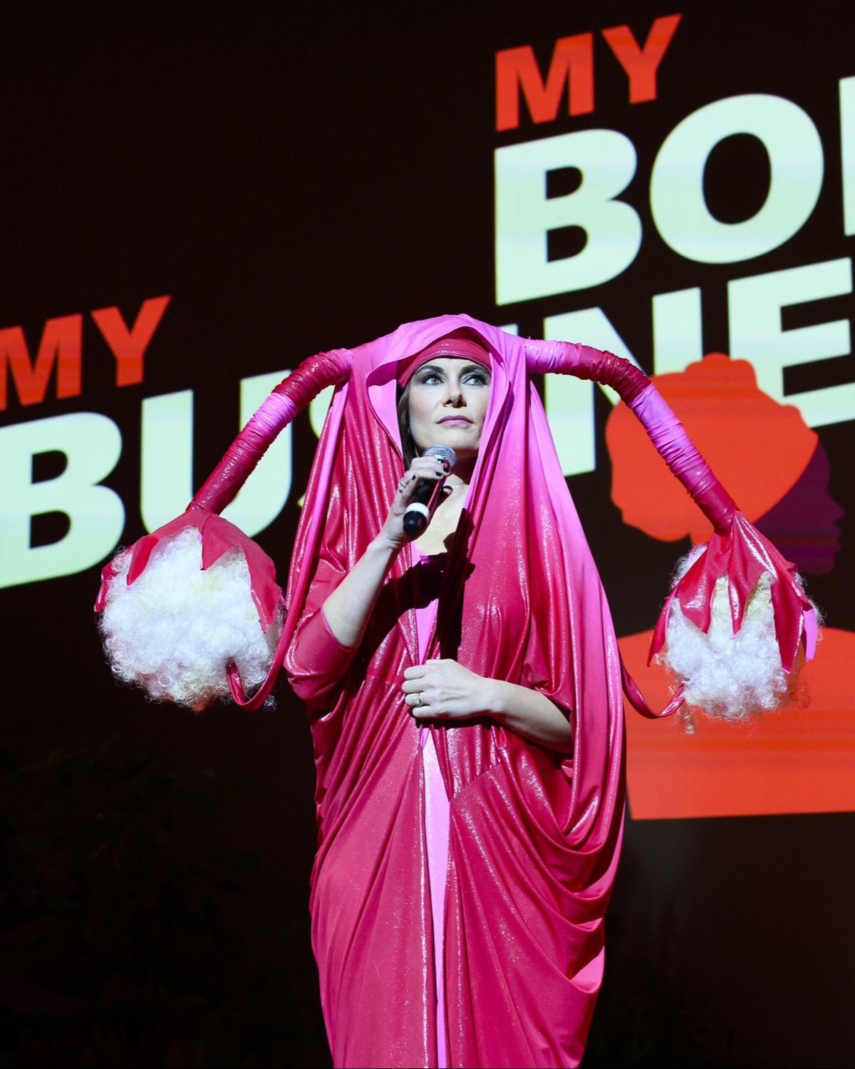 A performer in a sculptural pink costume beneath a ‘My Body, My Business’ backdrop